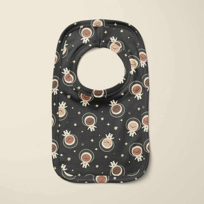 Pullover bib mockup featuring a dark fabric with a playful astronaut and star pattern, shown on a light neutral background.