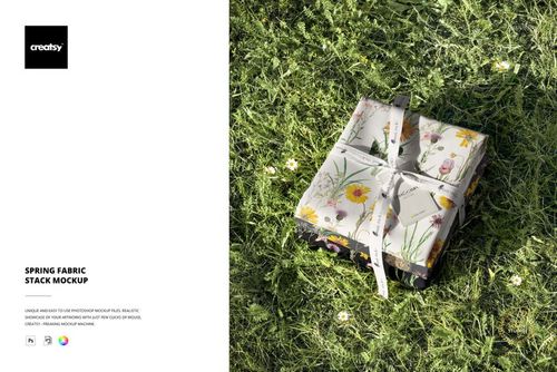 Spring fabric stack mockup showing multiple folded textiles with botanical prints, arranged on lush outdoor grass.