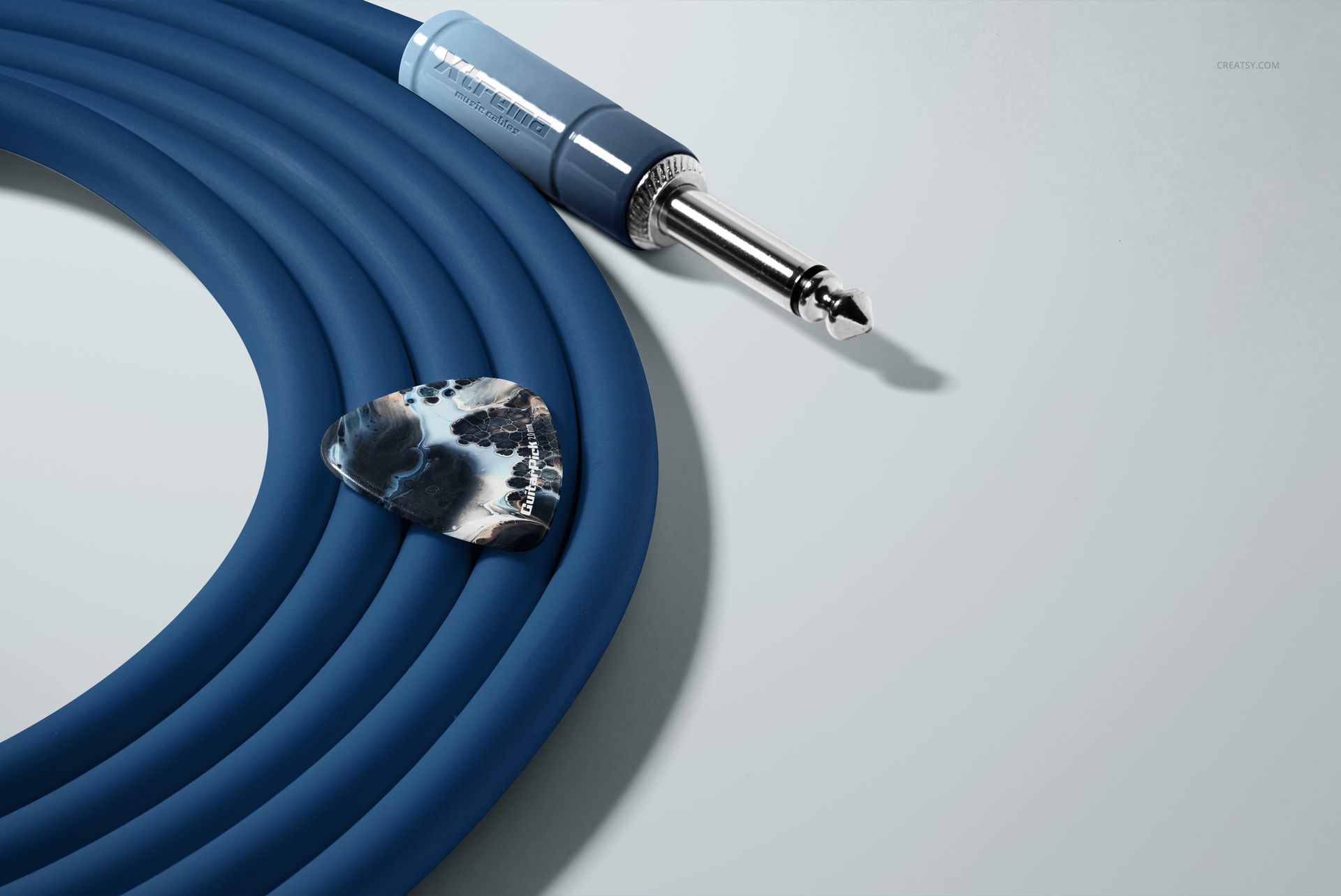Close-up view of a guitar pick and coiled blue jack cable arranged on a pale background in a PSD mockup.