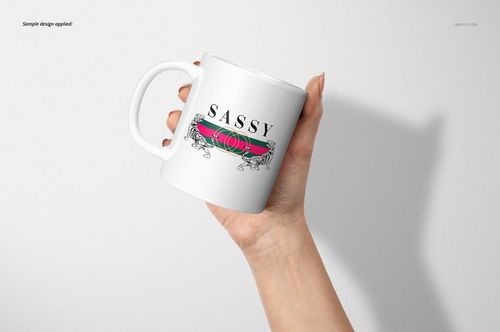 Hand holding a white 11oz mug with a colorful stripe and 'SASSY' text design, front view on light background.