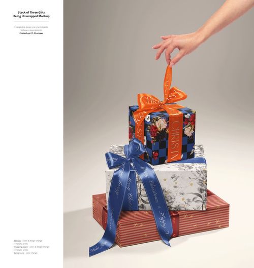 Hand untying ribbon on top gift box in a stack of Christmas presents, shown in a PSD mockup scene.