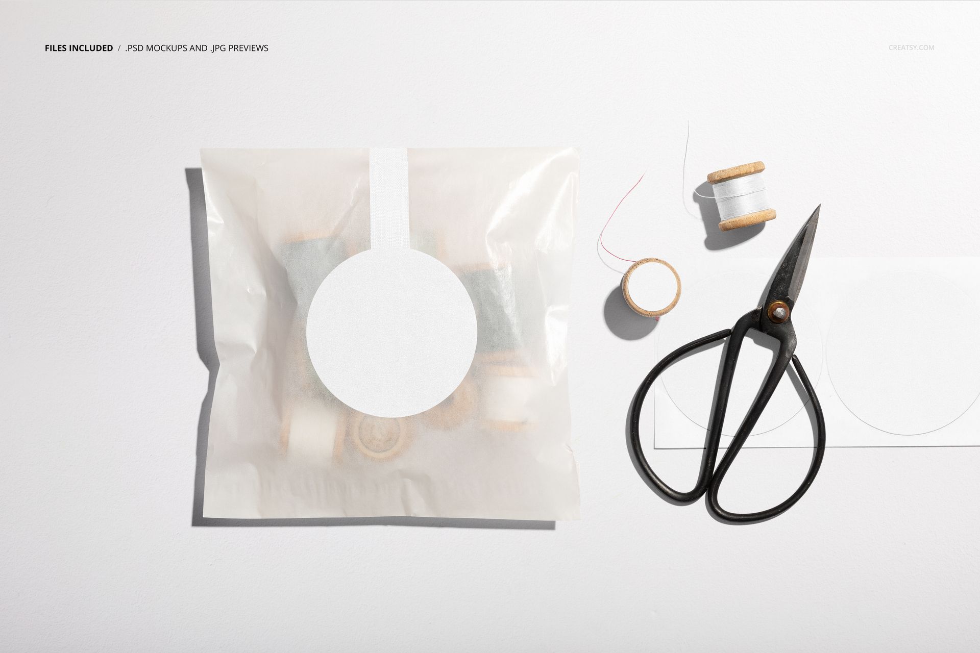 Mockup scene featuring a glassine packaging bag with sticker, spools of thread, scissors, and a blank label from above.
