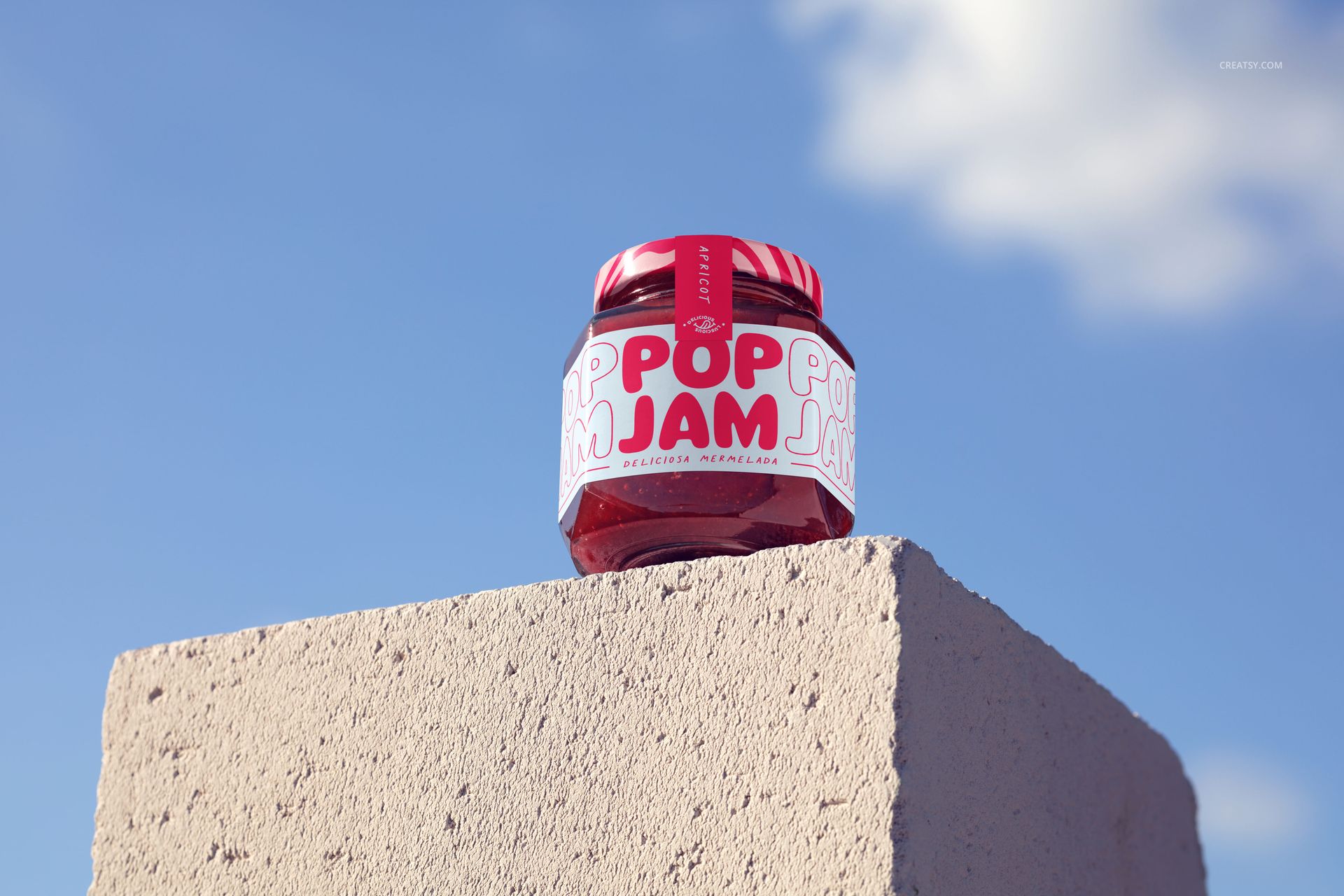 Front view of a jam jar mockup featuring a red lid and vibrant label, set outdoors on a textured stone block under clouds.