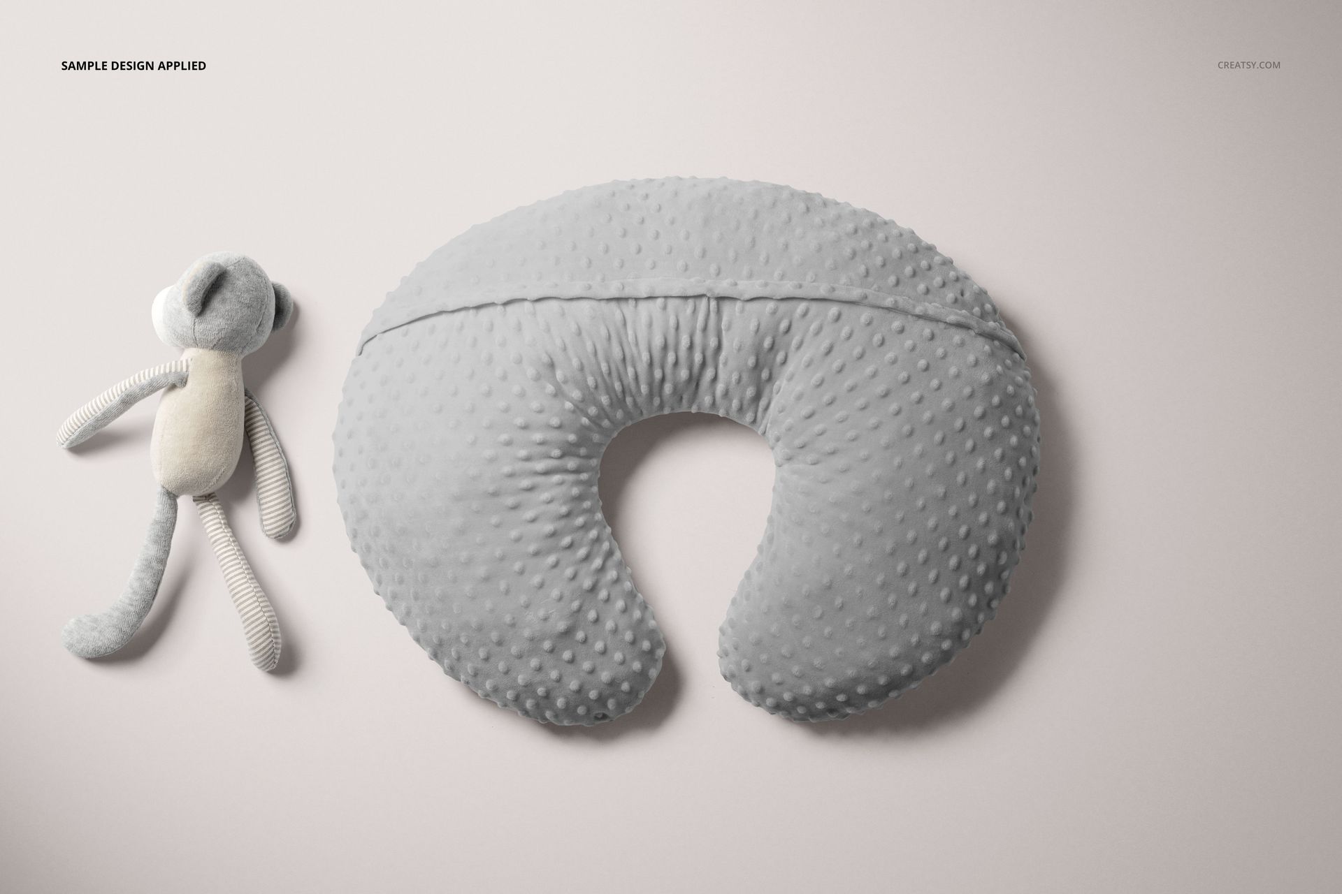 PSD mockup featuring a gray nursing pillow cover with raised dots, accompanied by a fabric stuffed animal on a neutral backdrop.