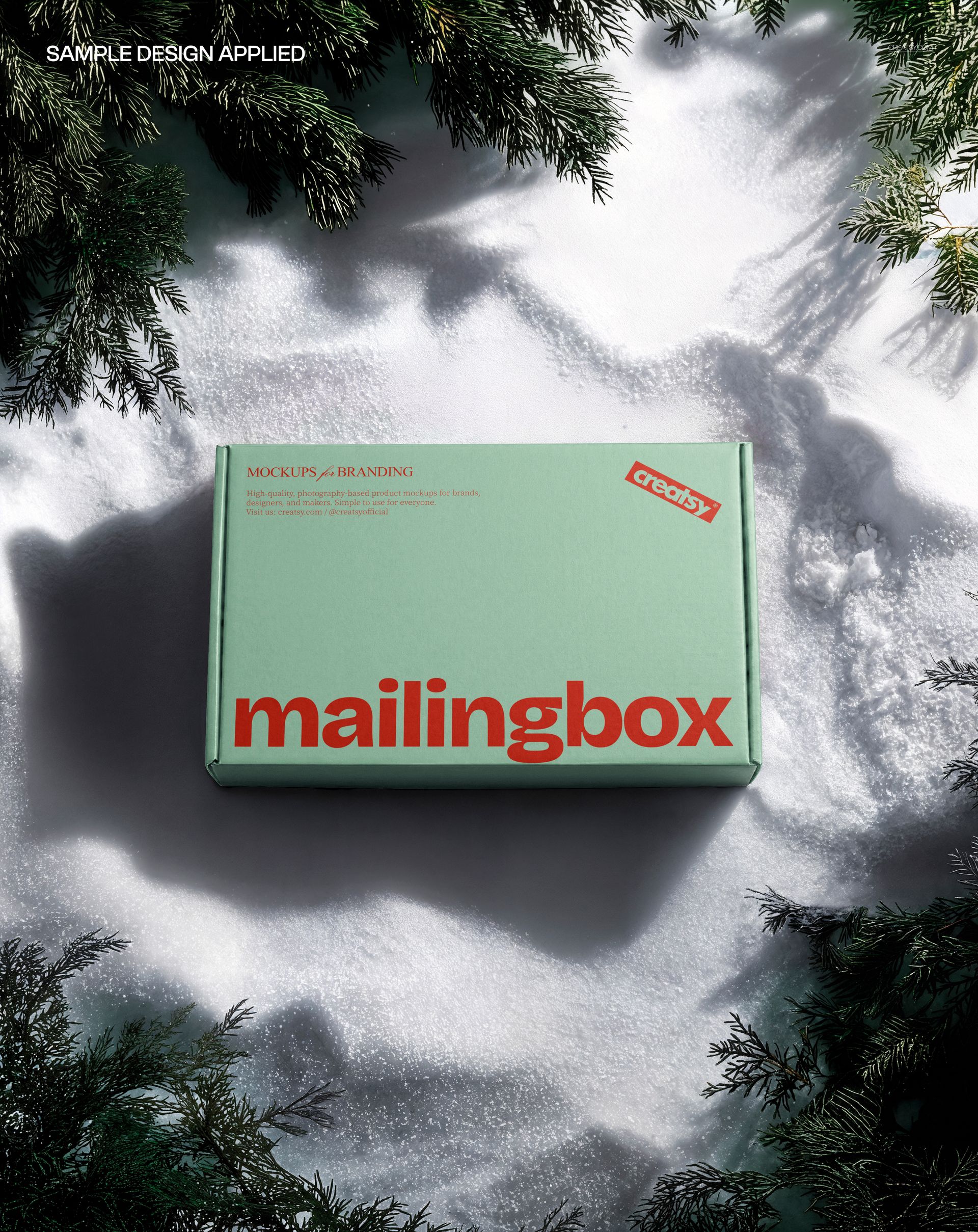 Mint green mailing box mockup resting on snow, framed by evergreen branches, viewed from above.