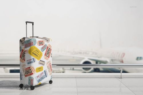 Mockup of a suitcase luggage cover with vibrant ticket motifs, shown in front of large windows overlooking an airplane.