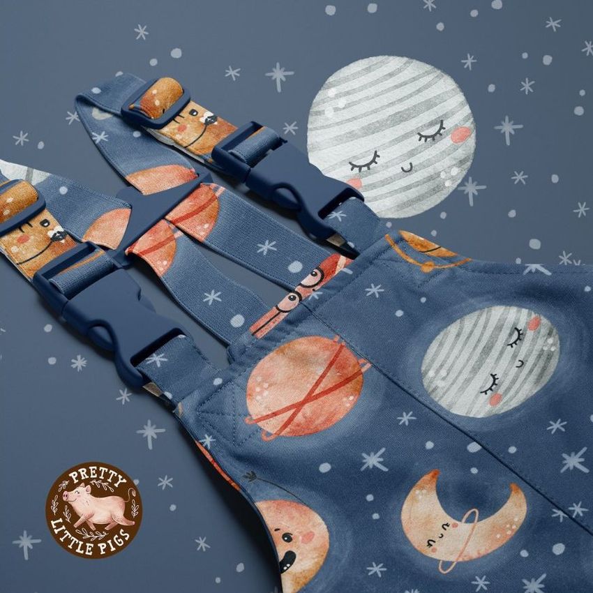 Kids rainwear mockup featuring blue overalls with playful planet and moon illustrations, shown on a blue background with stars.