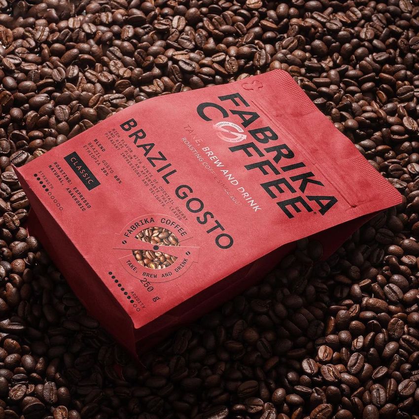 Coffee bag mockup featuring a red package with bold black text, placed on a surface covered with roasted coffee beans.