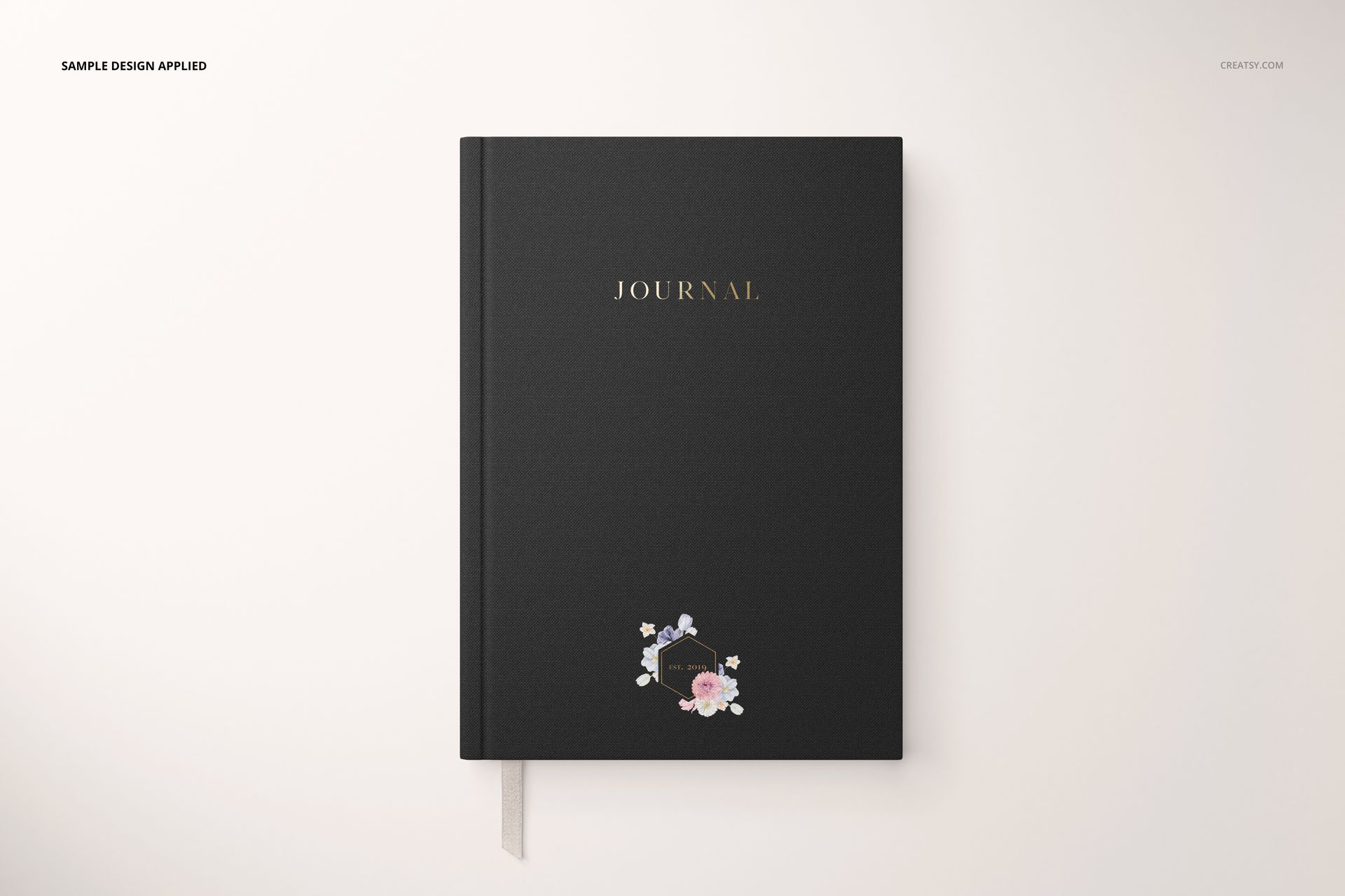Stationery set mockup featuring a black journal with gold text and small floral design, shown from above.