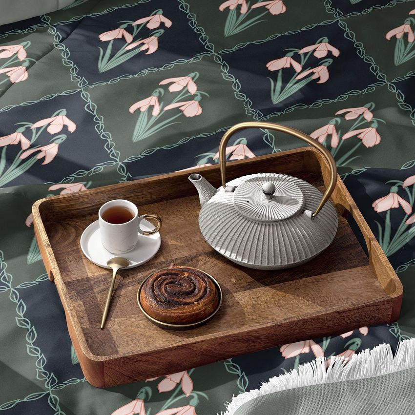 Microfiber comforter mockup featuring a wooden tray with a teapot, cup of tea, spoon, and pastry on a floral patterned bedding.