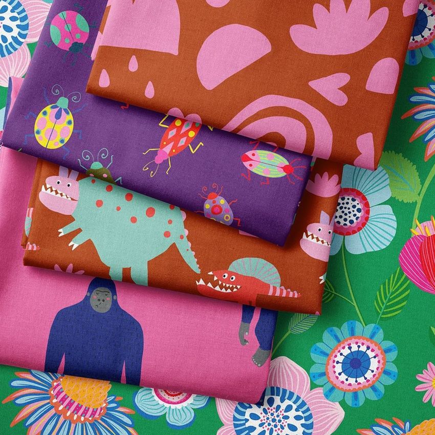 Folded fabrics mockup showing four colorful textiles with playful animal and floral patterns, arranged on a floral background.