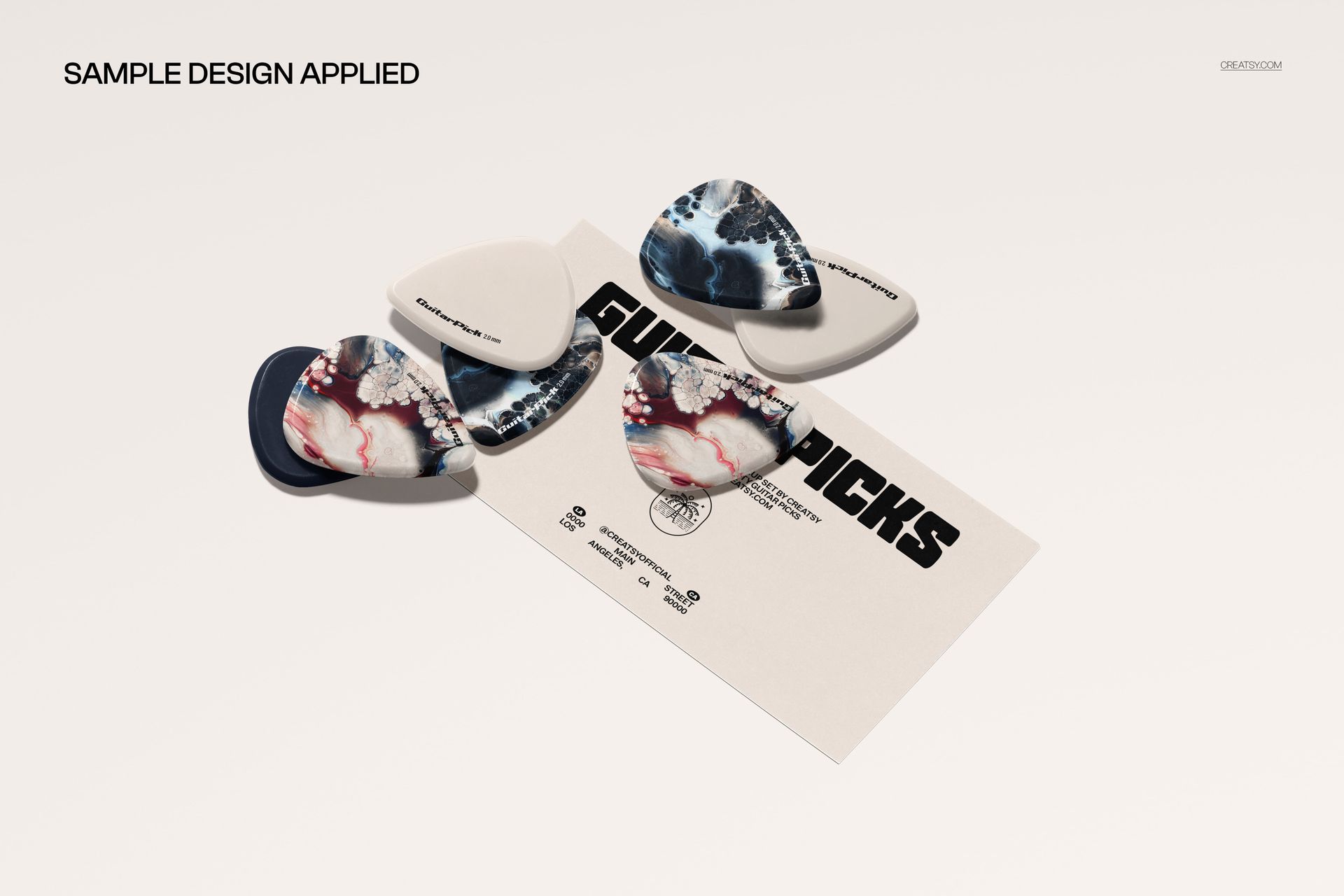 Front view of a business card mockup with several guitar picks in assorted colors and abstract patterns on a light surface.