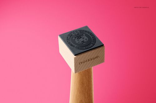 Single wooden stamp mockup with engraved black rubber surface, displayed upright on a pink backdrop in close view.