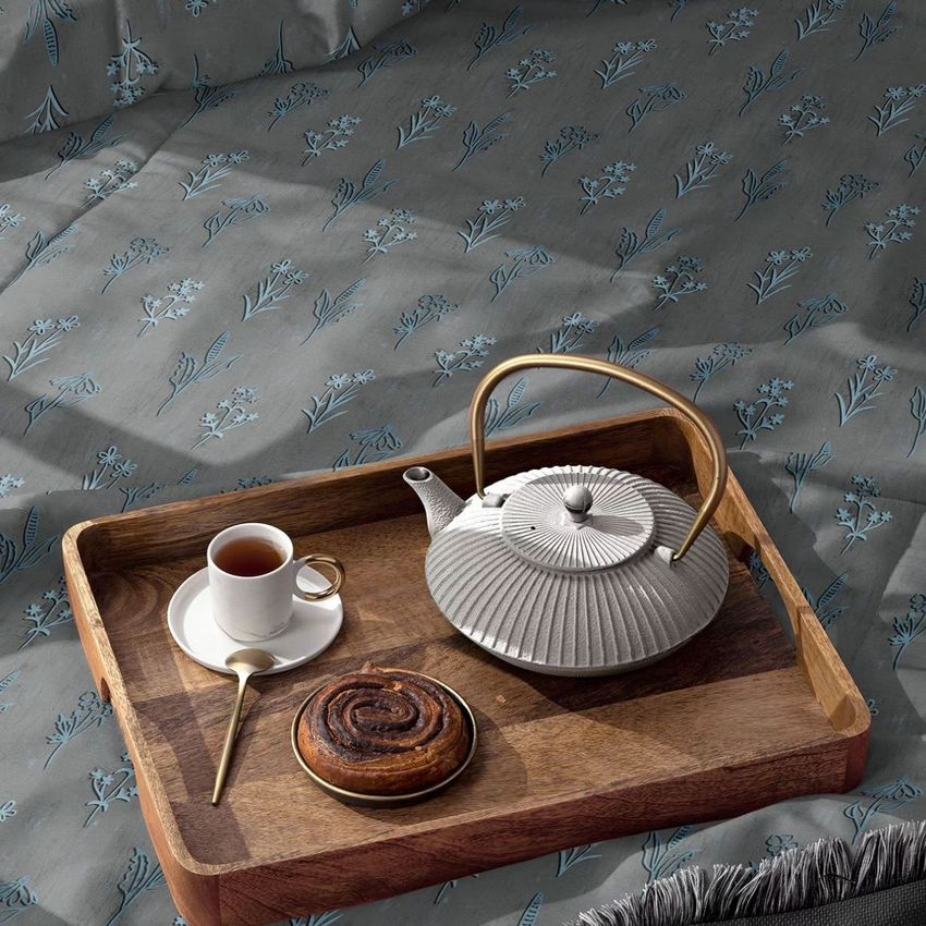 Microfiber comforter mockup featuring a wooden tray with a teapot, cup of tea, and pastry on a bed with a blue floral pattern.