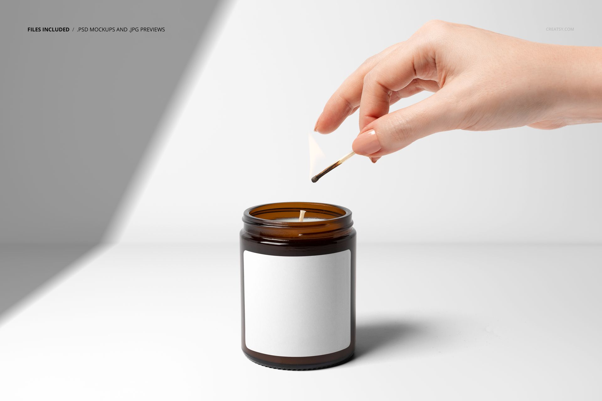 Amber glass jar candle with blank white label being lit by a hand holding a match, shown in a front view mockup.