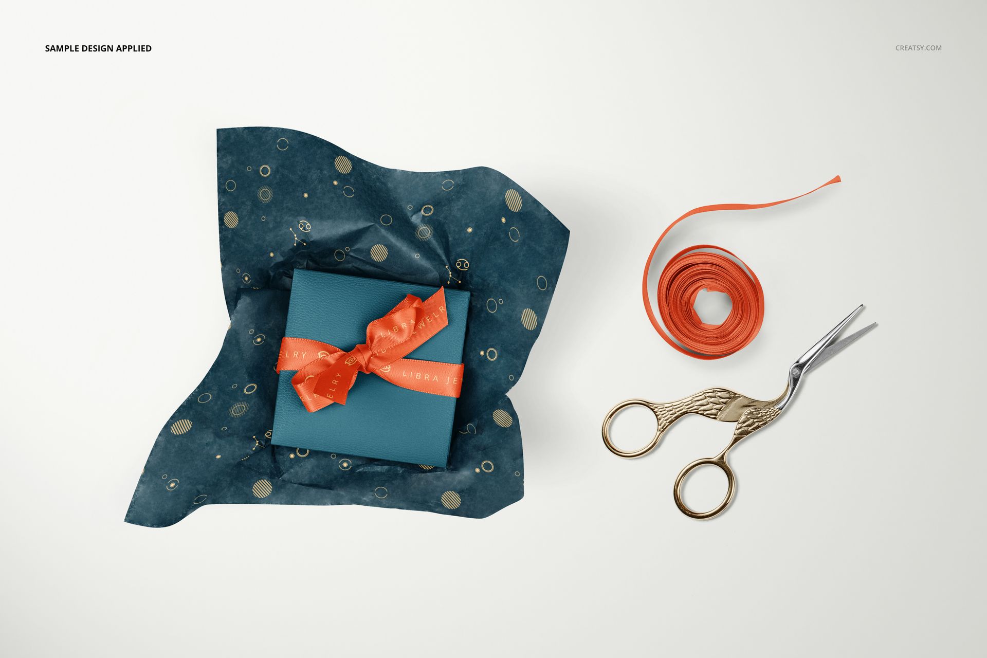 Mockup scene showing a gift box wrapped in patterned tissue paper, orange ribbon, and scissors arranged nearby.