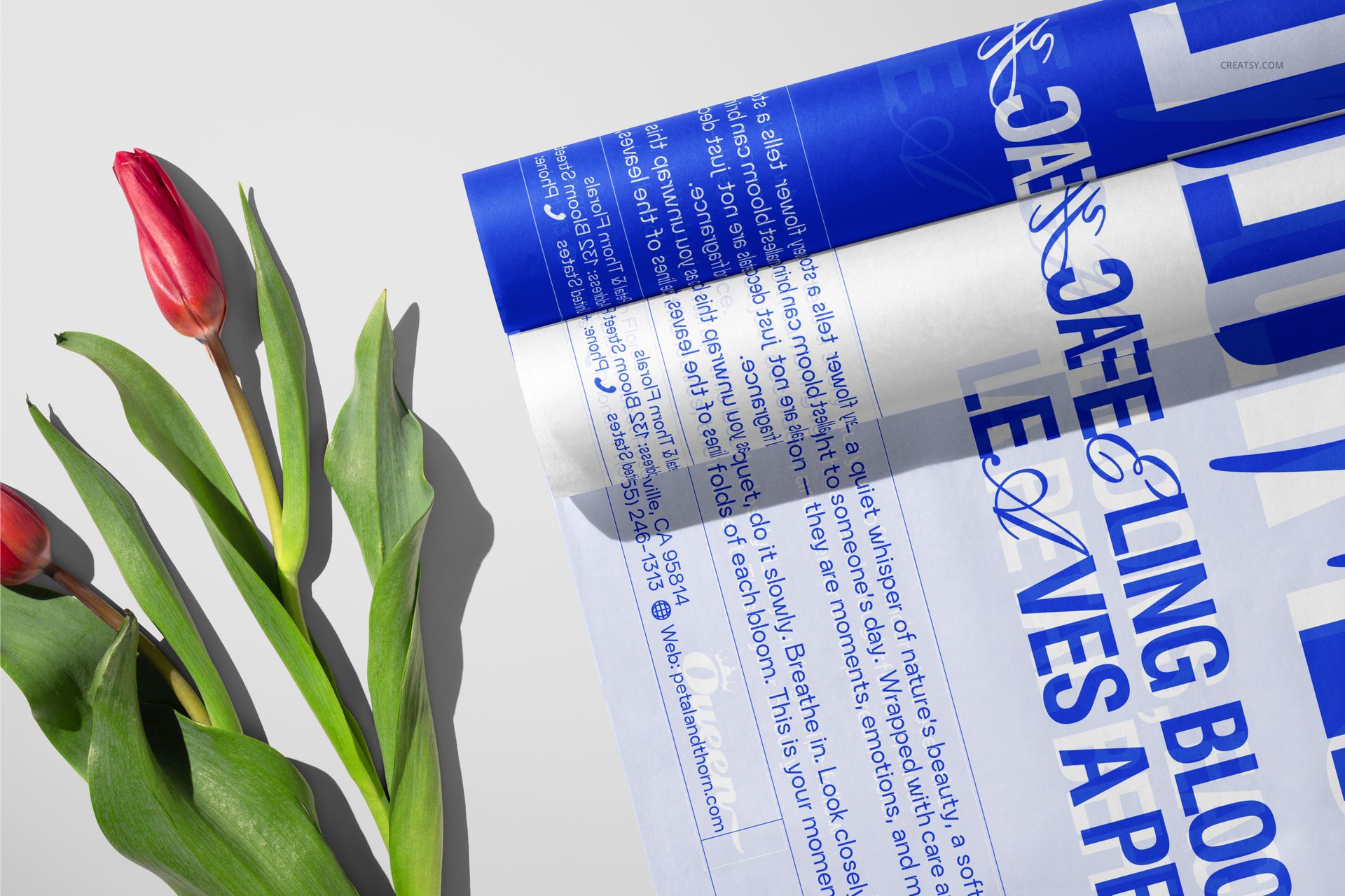 PSD mockup displaying tulip flowers alongside tissue wrapping paper with prominent blue typography, viewed from above.