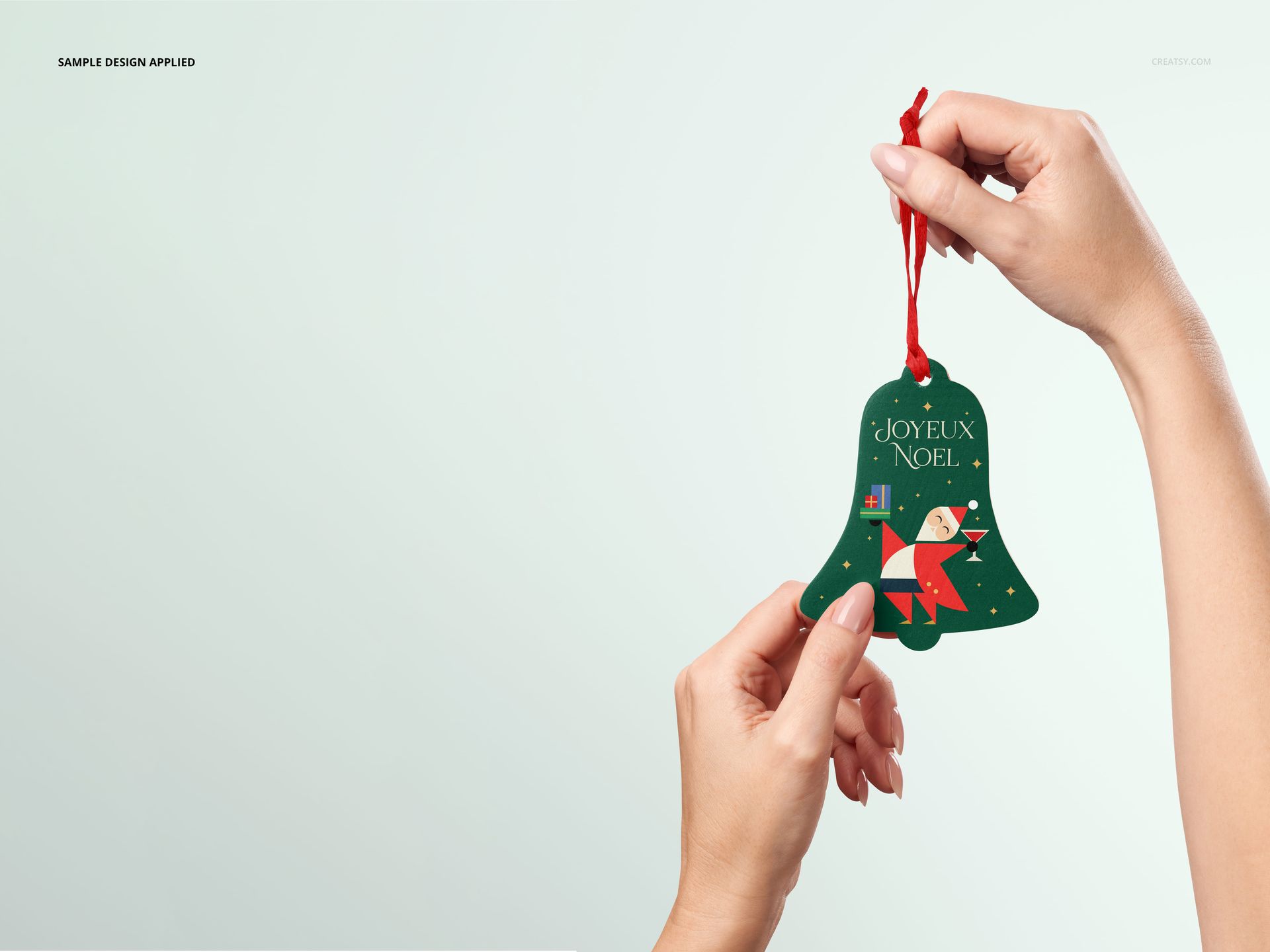PSD mockup showing a bell-shaped wooden Christmas ornament with a colorful print, held by hands against a light background.