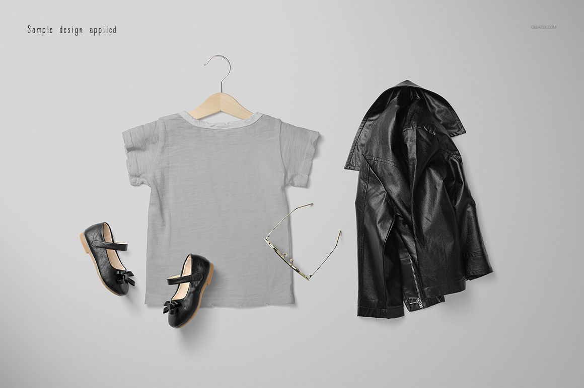Flat lay of a girls chic set mockup featuring a gray t-shirt on a hanger, black shoes, sunglasses, and a black jacket on a light background.