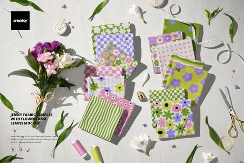 PSD mockup showing colorful jersey fabric pieces with floral designs, displayed with sewing accessories and green leaves.