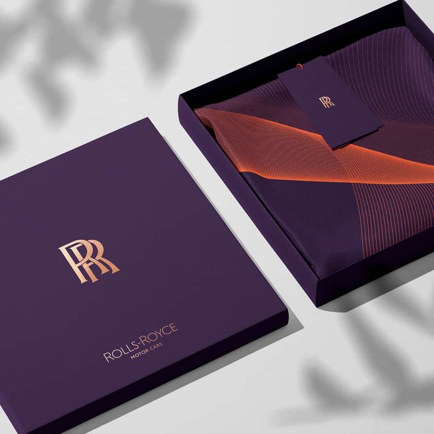 Silk scarf box mockup featuring a purple box with metallic gold logo, an open lid, and a folded scarf with an orange pattern inside.