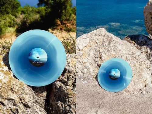 PSD mockup featuring a blue vinyl record on rugged coastal rocks with clear blue water and natural landscape visible.
