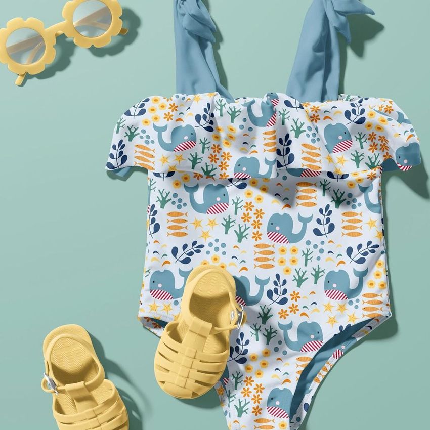 Baby swimsuit mockup displayed on a light teal background with yellow sandals and playful sunglasses as props.