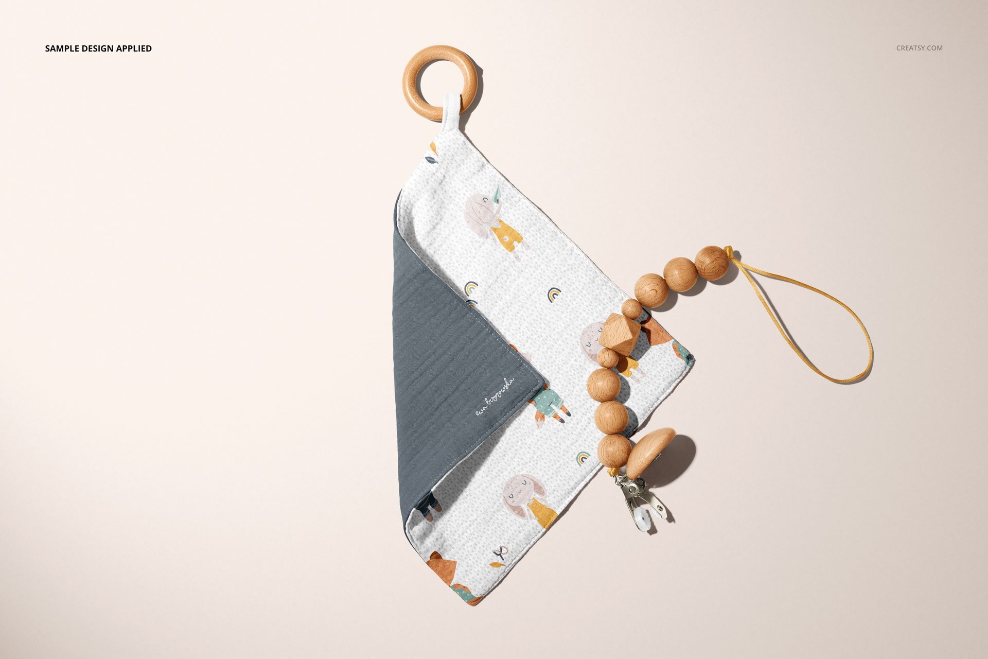 PSD mockup of a muslin swaddle and wooden teether set, displayed flat with soft colors and a simple background.