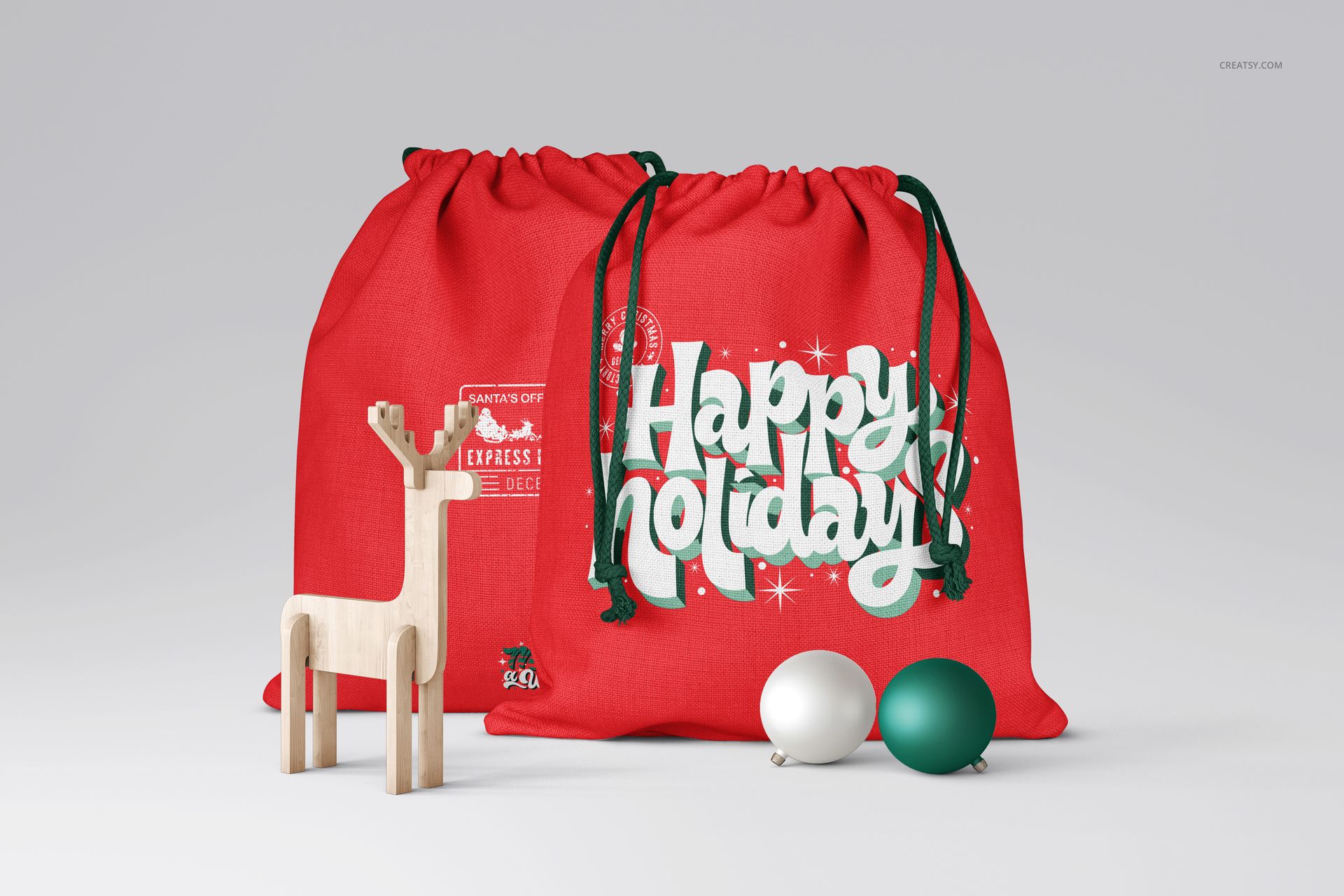 Christmas PSD mockup showing two red drawstring bags with holiday graphics, accompanied by a wooden reindeer and baubles.