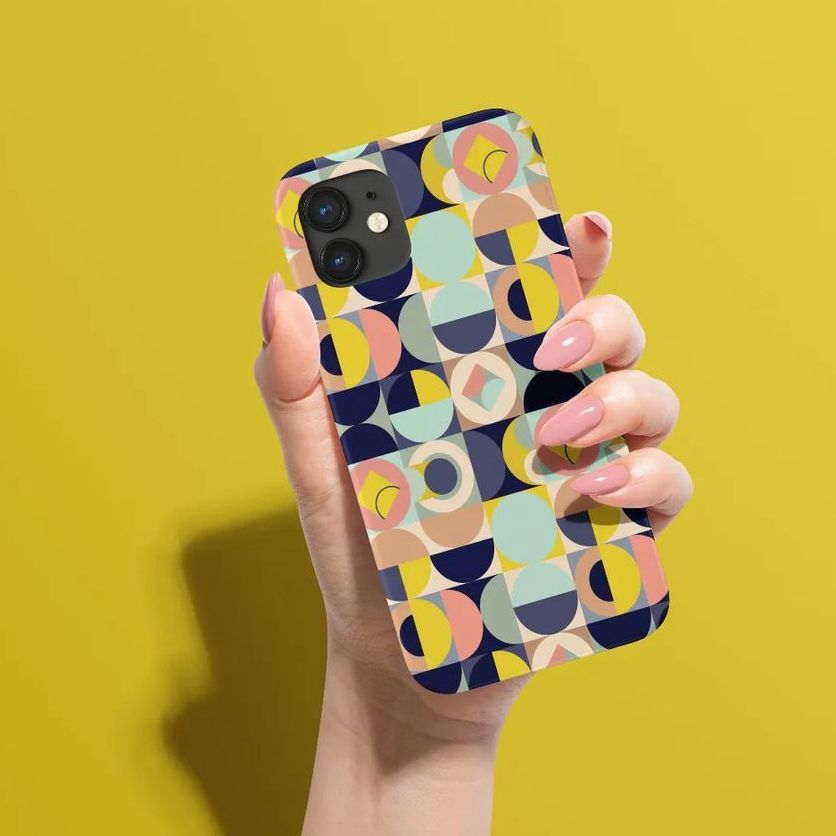 Hand holding an iPhone 12 matte snap case mockup with a colorful geometric pattern, set against a solid yellow background.