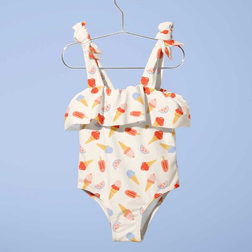 Baby swimsuit mockup featuring a white one-piece with colorful ice cream and fruit patterns, hanging on a metal hanger against a light blue background.