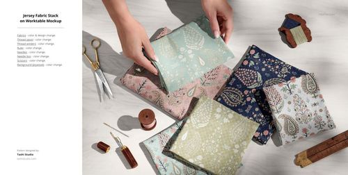 PSD mockup featuring folded jersey fabrics in various botanical prints, accompanied by scissors, thread, and pins in a creative workspace.