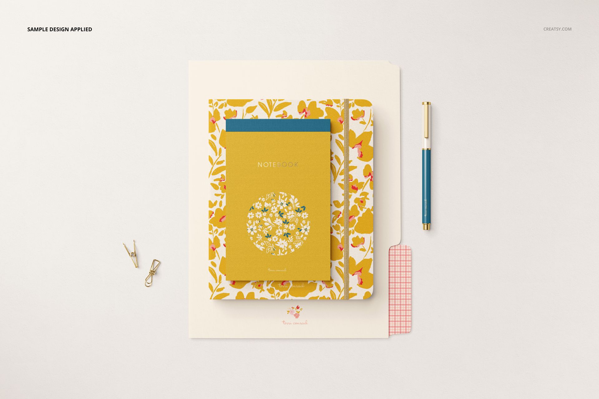Top view of a stationery mockup featuring a floral folder, yellow notebook, blue notepad, gold pen, and small paper clips.