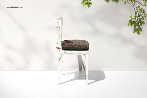 Rustic chair cushion mockup featuring a distressed white chair and a dark cushion with a subtle red pattern, side perspective.