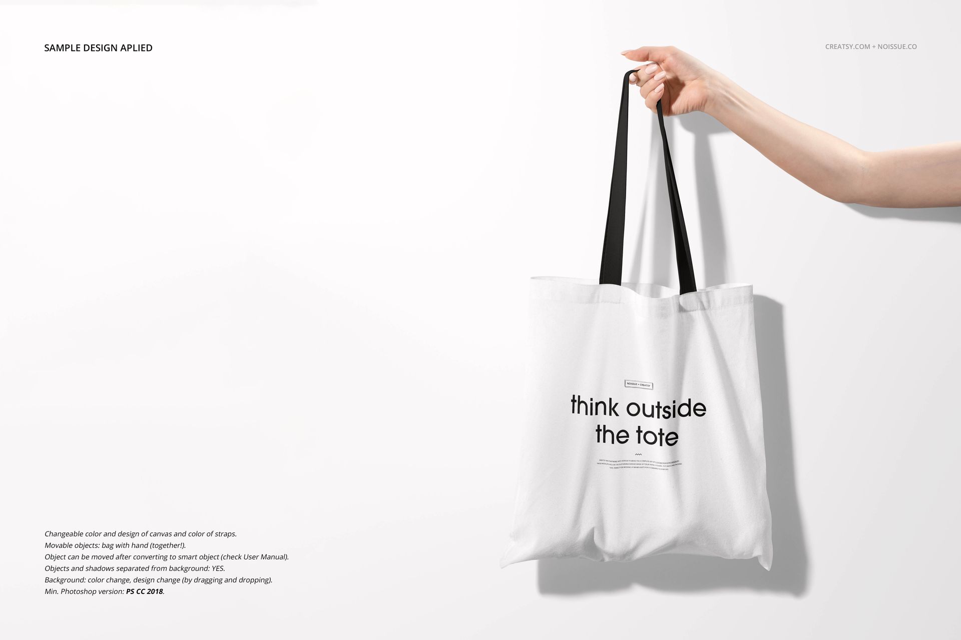 Front view of a white tote bag mockup with black straps, displayed with a hand holding it and text printed on the bag.