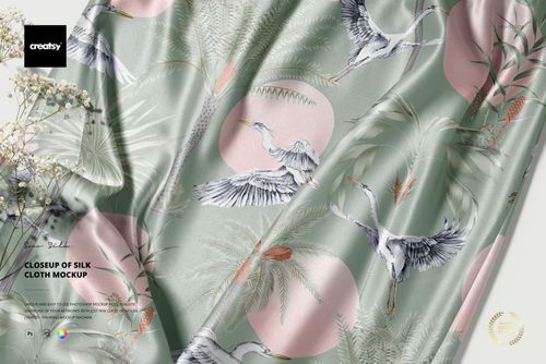 Twisted satin silk mockup with illustrated cranes, tropical leaves, and soft pink circles on pale green fabric.