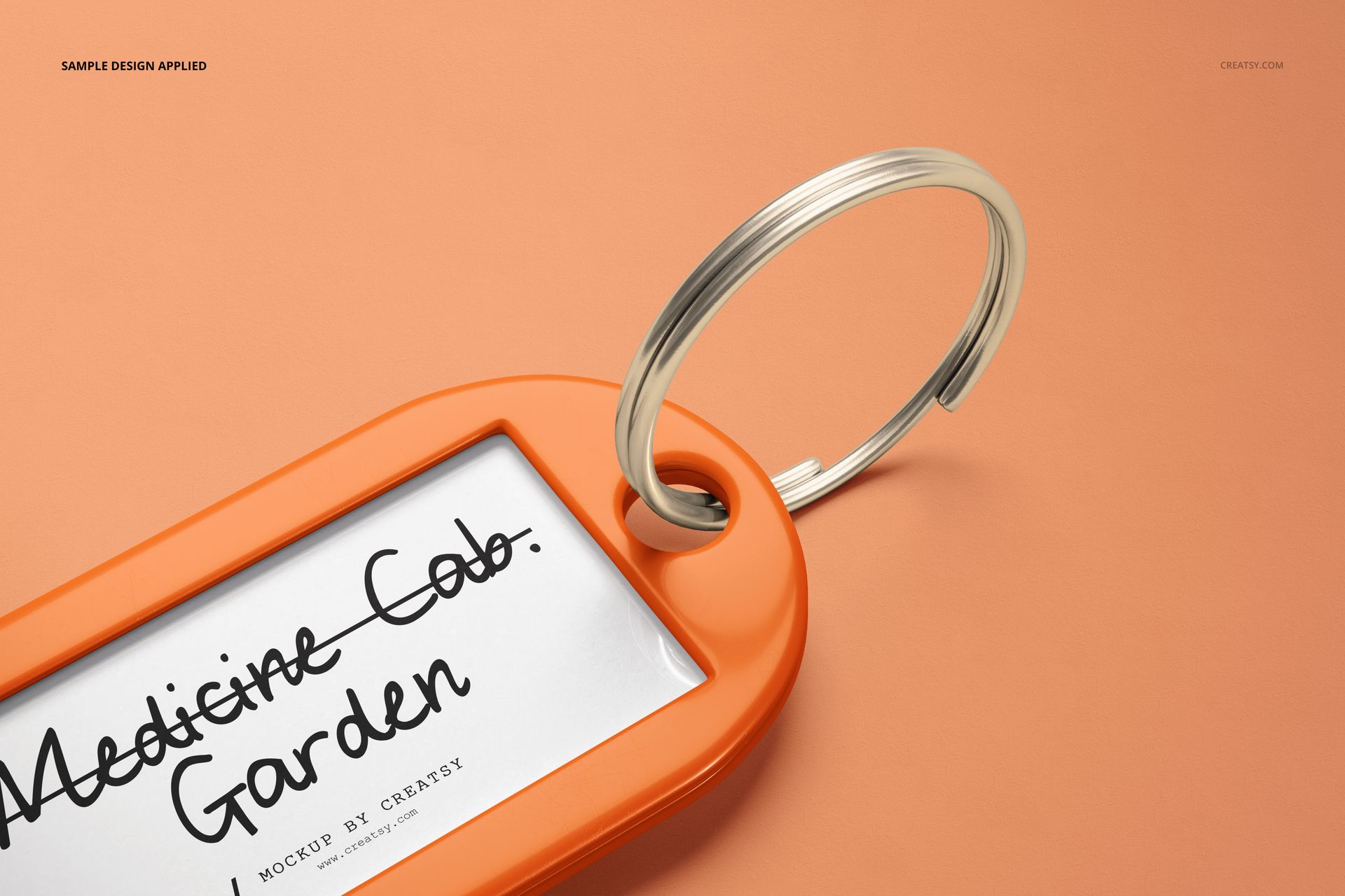 Close-up view of a key tag mockup set, showing an orange frame, metal ring, and white label on a peach background.