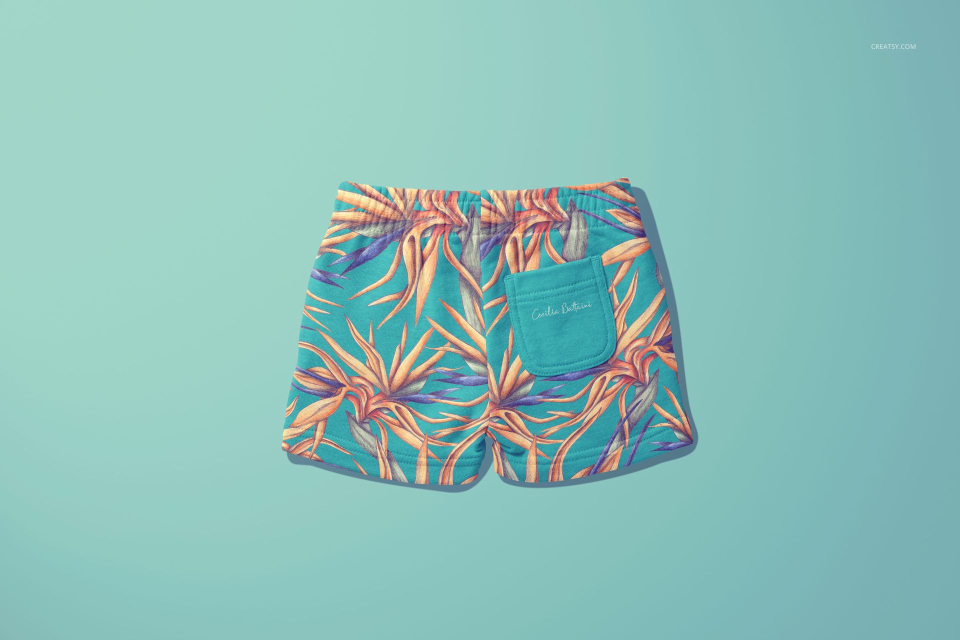 Kids shorts mockup featuring a vibrant floral design in orange and purple tones, laid flat against a blue backdrop.
