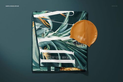 Beach towel mockup featuring a green leafy design, neatly folded and paired with an orange swim cap on a flat background.