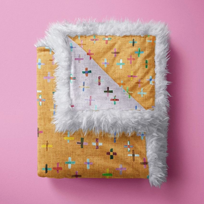 Sherpa baby blanket mockup featuring a folded yellow blanket with colorful cross patterns and white faux fur trim on a pink background.