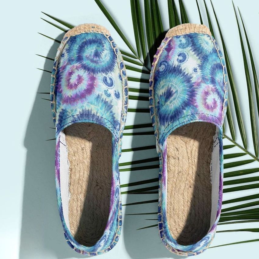 Canvas espadrilles mockup featuring a pair of shoes with vibrant blue and purple tie-dye patterns, displayed on a light surface with palm leaves.