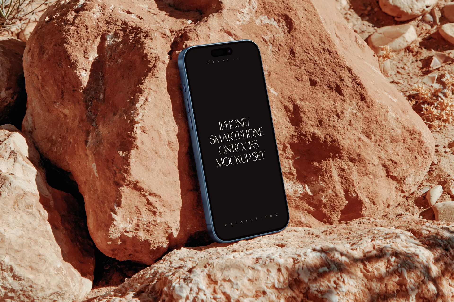 iPhone smartphone mockup with dark screen leaning on rugged rocks, photographed from a front angled perspective.
