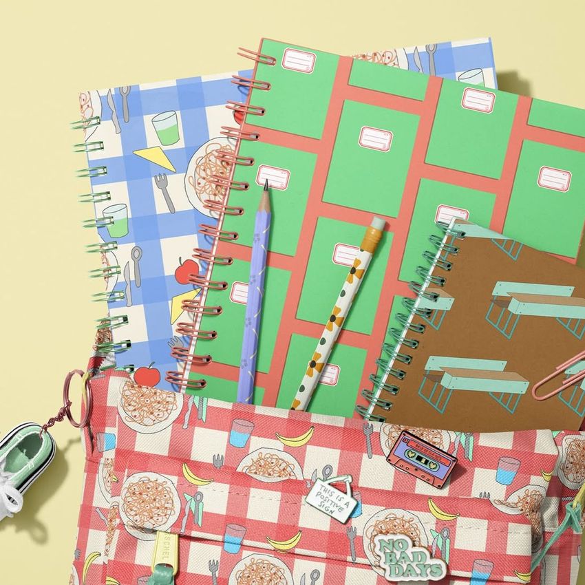 School backpack with a red checkered pattern is filled with three spiral notebooks featuring colorful macaroni and geometric designs.