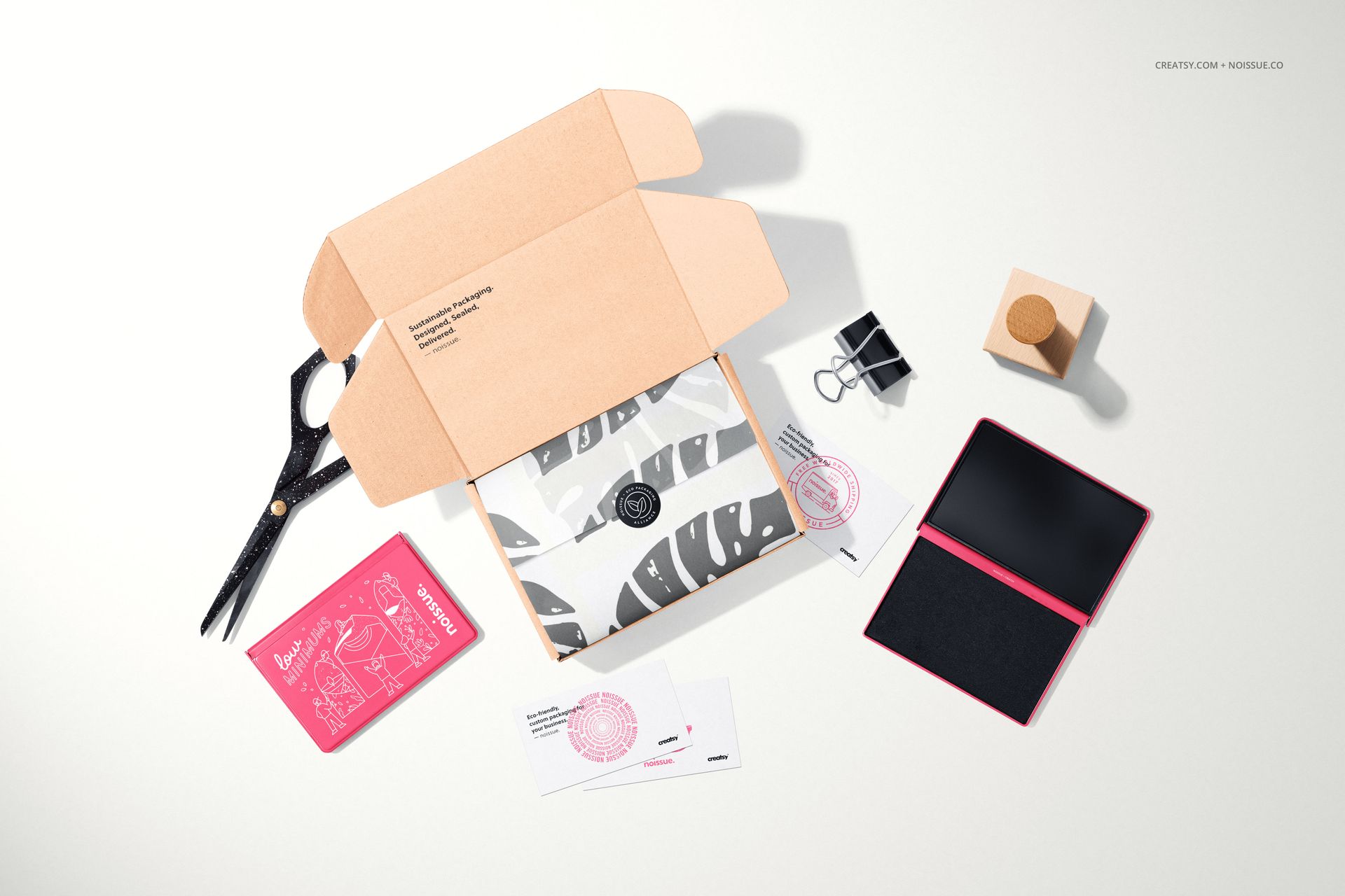Flat lay of a stationery mockup set featuring a wooden stamp, open box, ink pad, scissors, and printed cards.