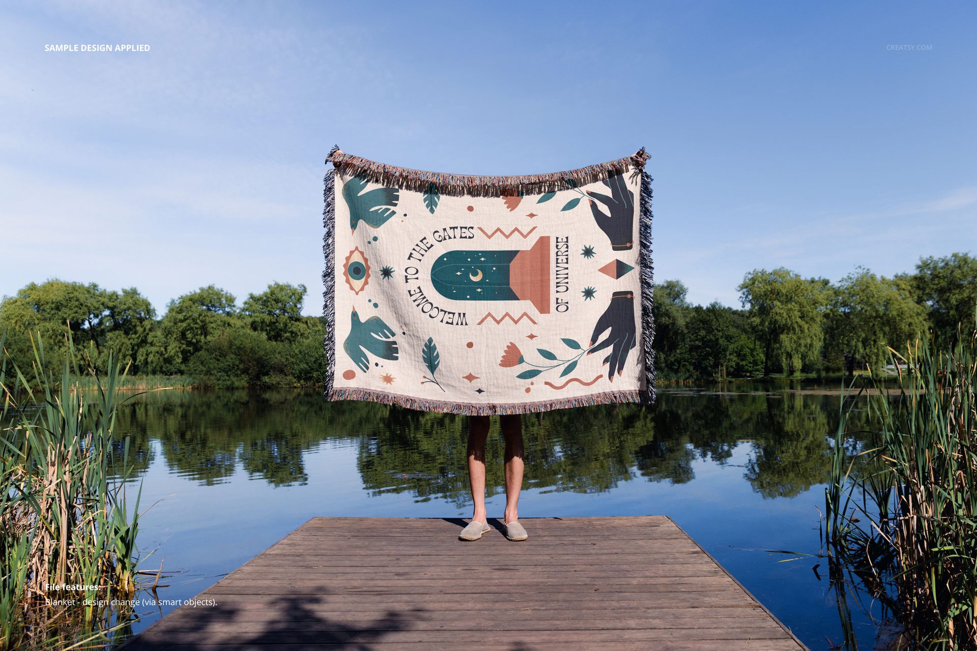 Jacquard fringed woven throw blanket mockup displayed outdoors, held by a person on a dock with calm water and greenery.