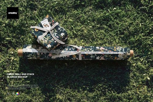 Floral patterned fabric roll and folded bundle arranged on grassy ground, top-down perspective, PSD mockup style.