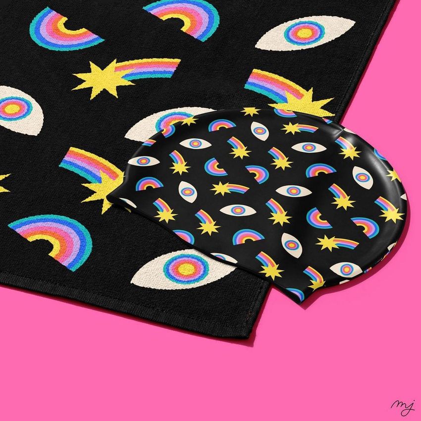 Swim cap mockup featuring a black cap with colorful rainbow, eye, and star patterns placed on a matching patterned towel.
