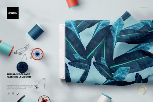 PSD mockup displaying a patterned fabric bolt next to assorted thread spools and sewing accessories on a pale background.