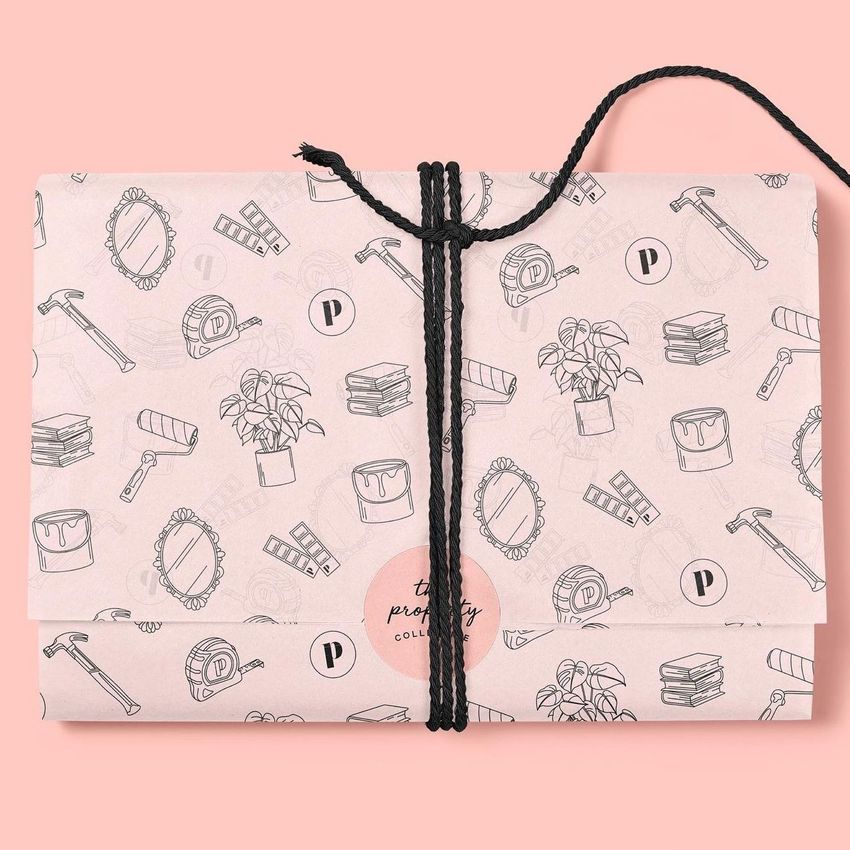 Tissue paper mockup featuring a folded package wrapped in black string, decorated with hand-drawn icons on a pink background.