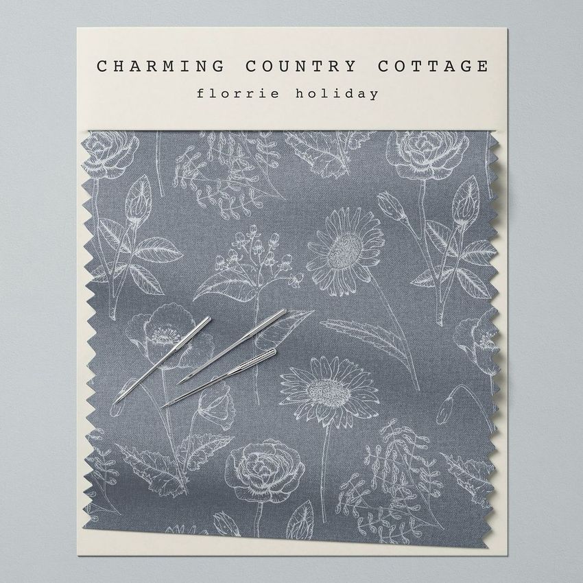 Fabric swatch mockup featuring a gray textile with white floral line art, displayed on a light background with sewing needles.